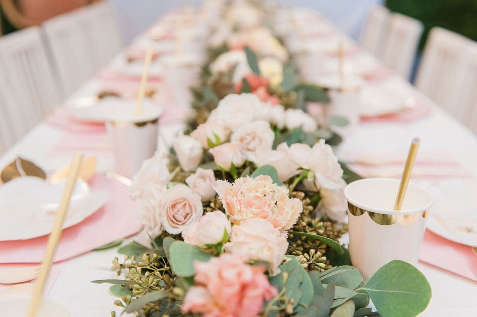 A beautiful table scape with pink and gold plates, flowers, napkins, and cups