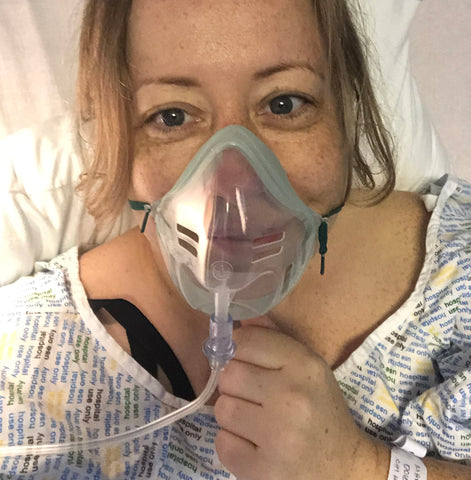 Mhairi, white female, smiles from behind oxygen mask after surgery.