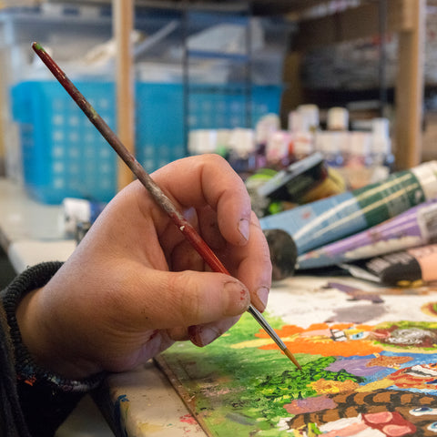 A photo of Ashlea's hand holding a paintbrush over one of her paintings.