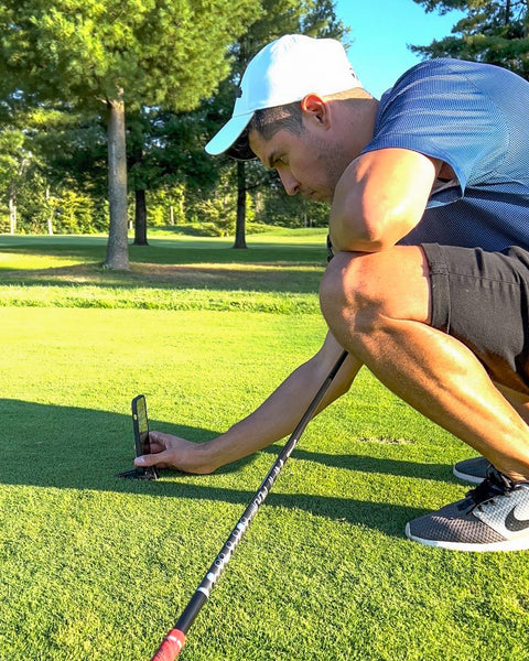 A man setting up a phone tripod on a golf course