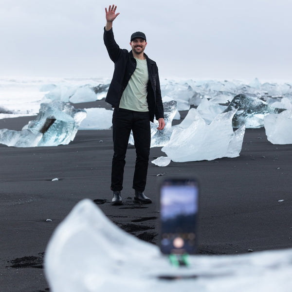 A man standing and rising his hand while a phone is taking a picture of him