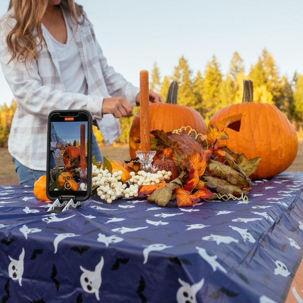 A women carving a pumpkin on a table in nature while being filmed with an iPhone
