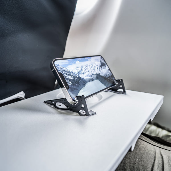 An Iphone on a tripod stand on the small table in an airplane