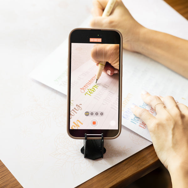 An iPhone on a tripod filming someone drawing