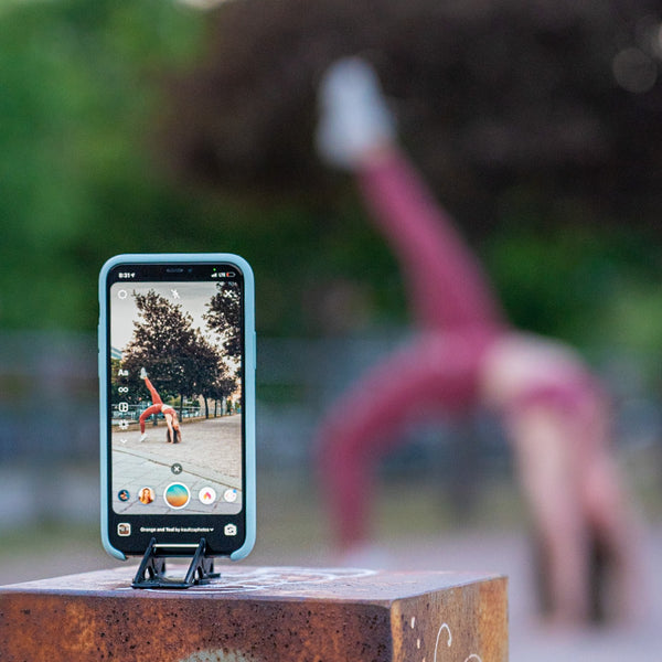 An iphone on a tripod stand taking a video of a girl doing gymnastic on the background