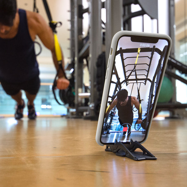 A tripod holding a phone taking picture of a man working out at the gym