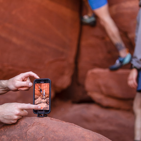 Someone taking a video from an iPhone on a tripod stand of a person climbing on red rocks