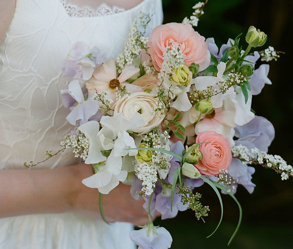 Model is holding an airy spring bouquet in pastel colours of peach, lilac, blush and white