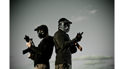 Two airsoft players stand back to back in army uniforms and full face helmets