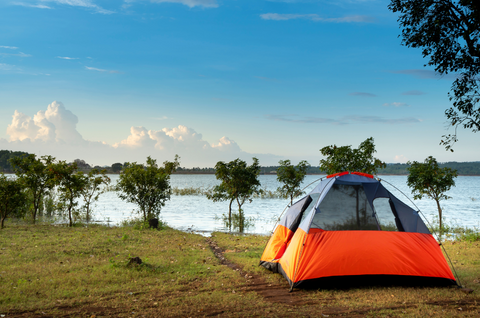 Orange tent in field beside lake