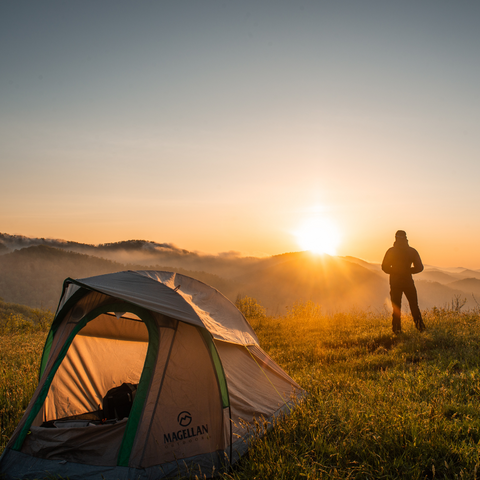 Man watches sunset in field beside a tent