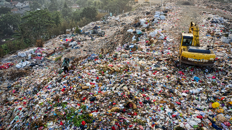 Huge landfill full of rubbish and discarded clothes with a yellow digger