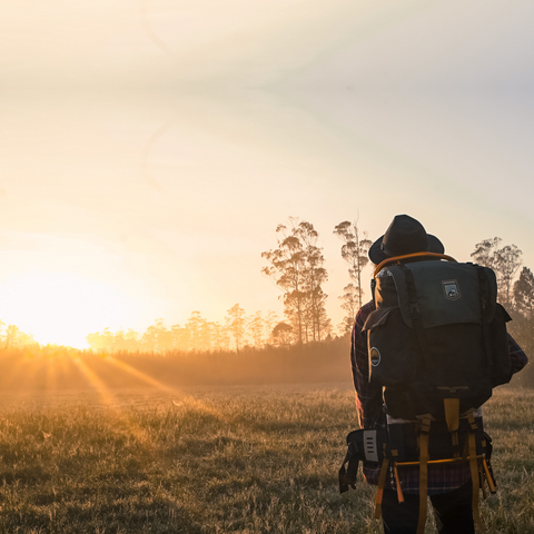 Man with large camping backpack looks ahead at sunrise