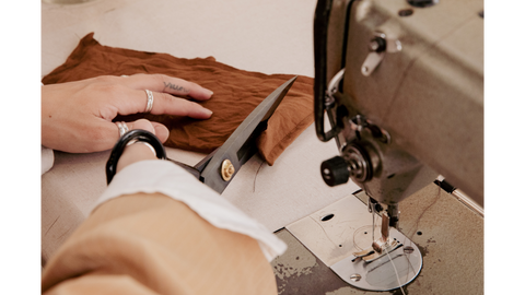 Artisan craftsperson cutting into a piece of fabric next to a vintage sewing machine