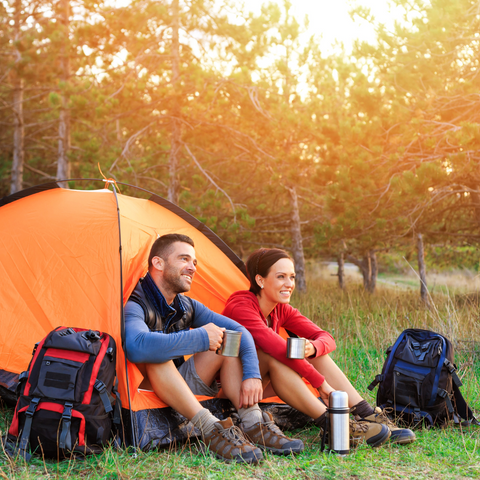 couple smile beside backpacks outside tent