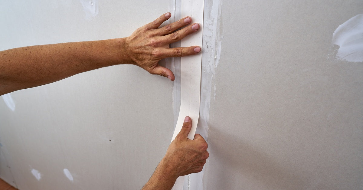 A focus shot of a pair of hands smoothing down a fresh piece of drywall tape to hide a drywall seam.