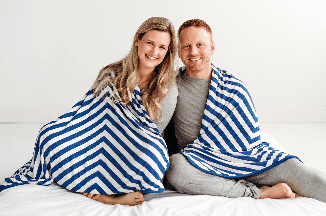 Two adults sitting and sharing the Classic Chevron Oversized Cloud Blanket draped around their shoulders.