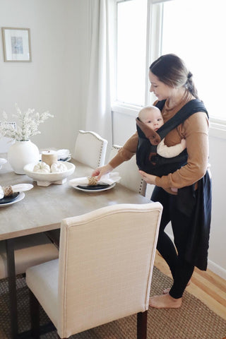 woman wearing a baby setting the table