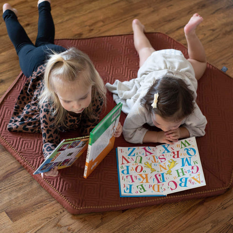two toddler girls laying on the ground reading books