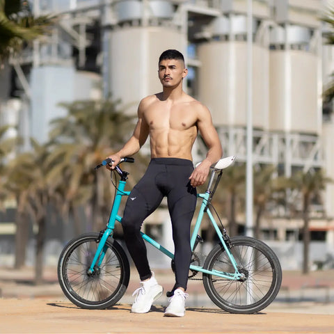 Compression men's leggings in solid black modeled by a shirtless man posing with a teal bicycle.