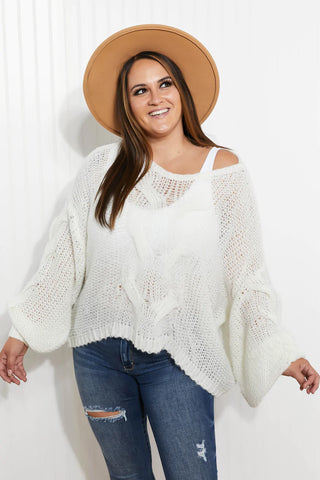 Woman wearing white sweater, denim jeans, fedora while smiling