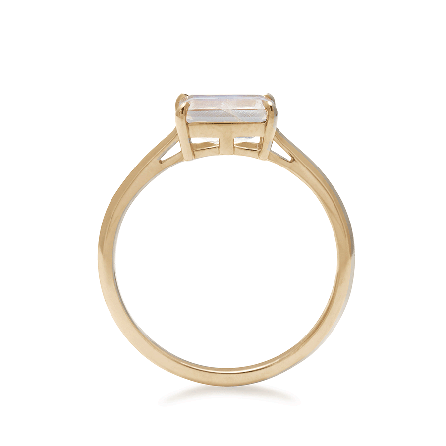 A side view of an east/west solitaire ring with an emerald shape rainbow moonstone set in yellow gold.