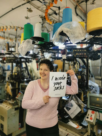 Anikó from the J Alex Swift team holds a sign saying "I made your socks"