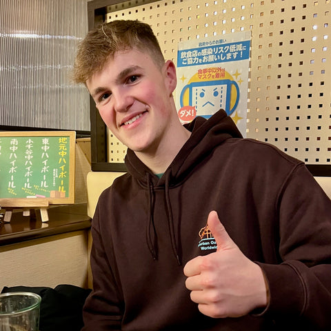 A picture of Bradley Rubra, who is the first employee at Byer Koi Farm.  This is a portrait picture of Bradley , with Bradley giving a thumbs up.  Bradley is sitting in a restaurant which you can see in the background.