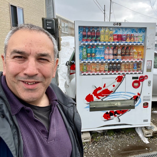 A selfie of myself, standing in front of a vending machine which is painted with pictures of koi.