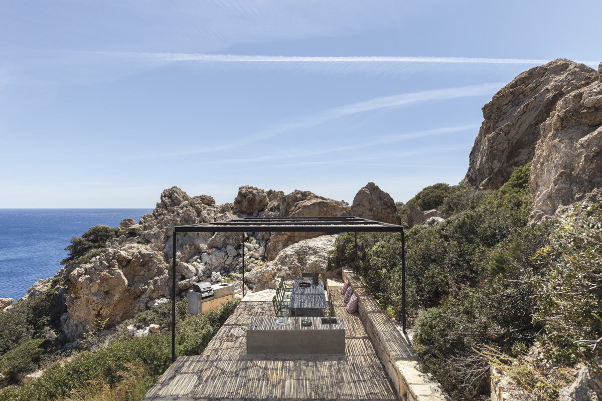 A través de un espacio abierto la casa se conecta con una gran terraza al aire libre en la parte más baja del lugar, donde se esconde otra de las múltiples vistas a la calma del mar. En la foto inferior se ve claramente el exterior de la propiedad hecha de hormigón visto, contrastando con los interior suaves y ligeros.