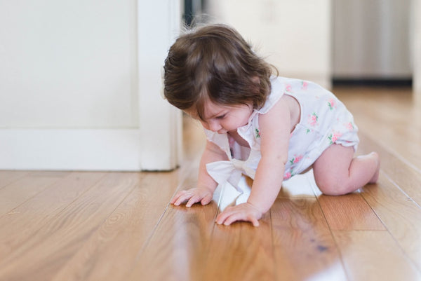 Baby in a dress crawling on a wood floor