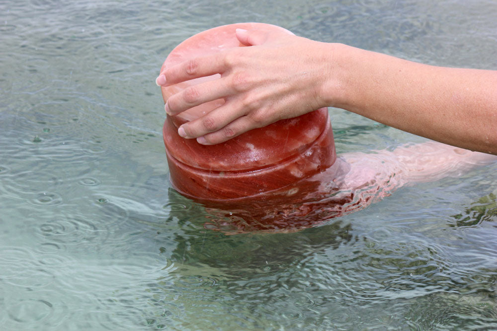 Himalayan rock salt urn being placed in water by two hands. 