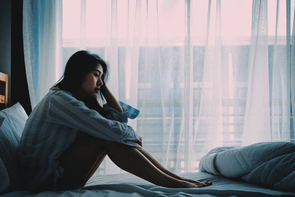 woman looking sad sitting on bed with her head in her hands