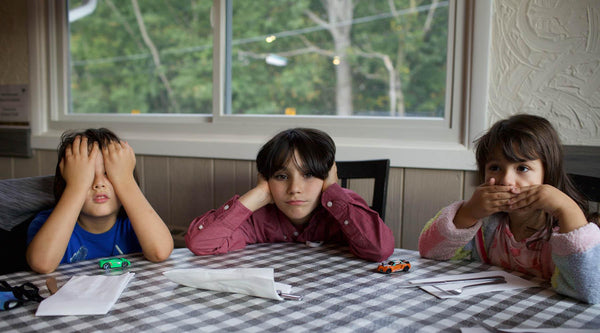 Three kids sitting at the kitchen table. Image by Keren Fedida on Unsplash.