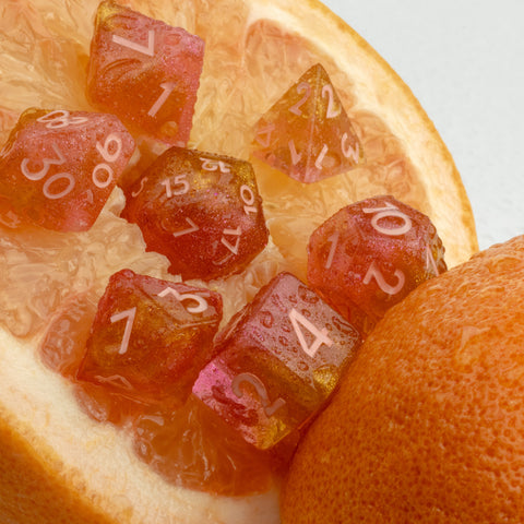 Orange resin dice set nestled in a grapefruit with a white background.