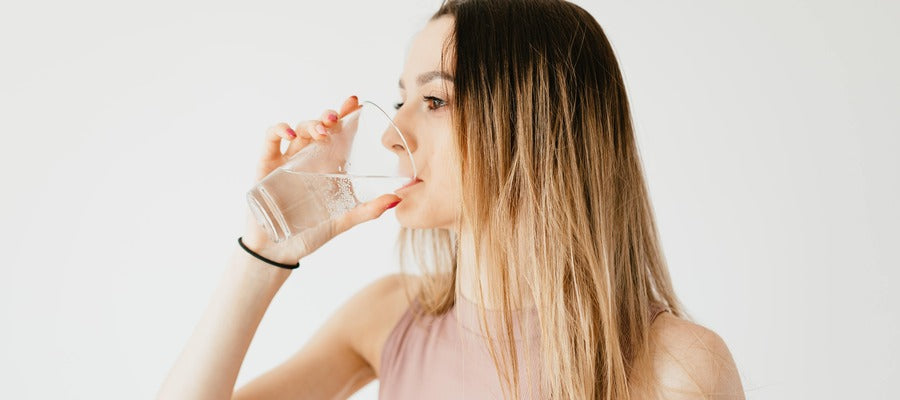 Mujer joven bebiendo agua de un vaso contra el fondo blanco.