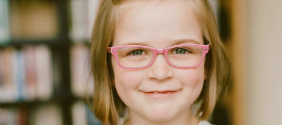 pale little girl wearing pink eyeglasses and smiling slightly