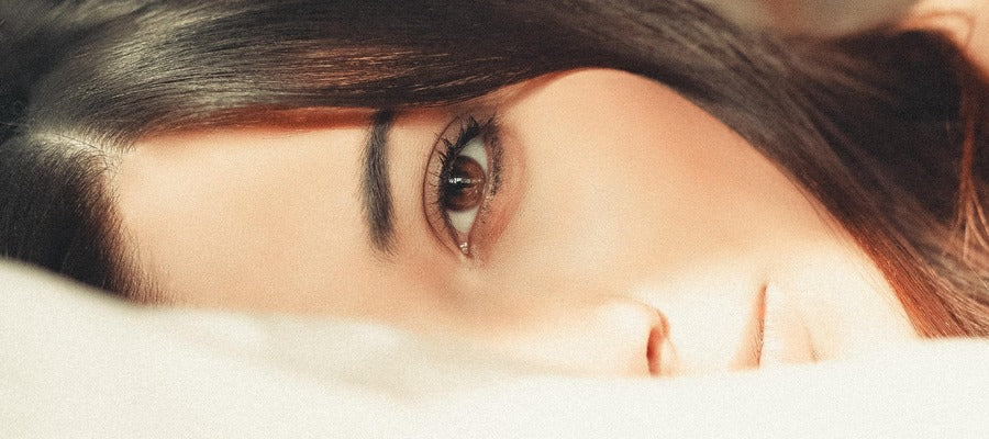 closeup portrait of one half of a woman's face lying on white sheets with her eye open