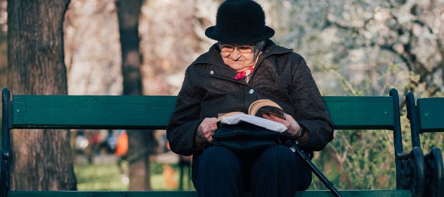 Anciana con gafas y sombrero leyendo un libro en un banco del parque verde