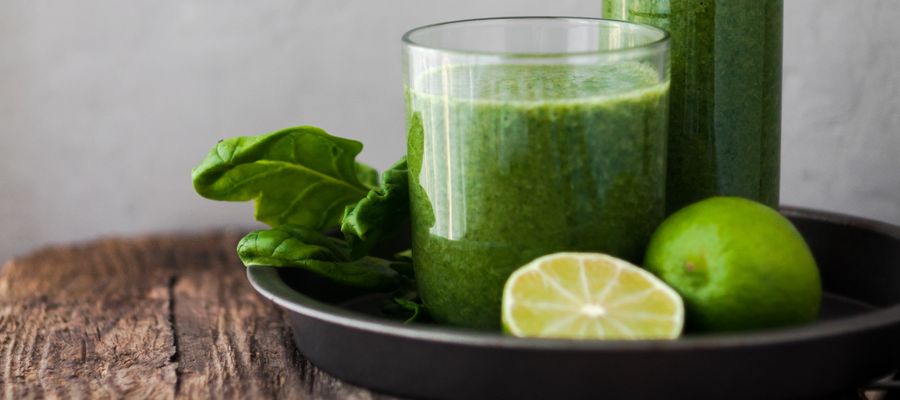 batido verde en un frasco sobre una bandeja redonda en una esquina de una mesa de madera