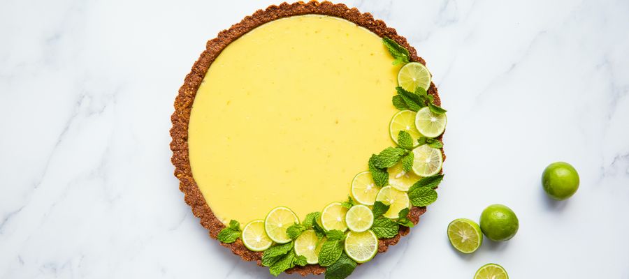 key lime pie on marble surface with lime slices and halved limes next to it