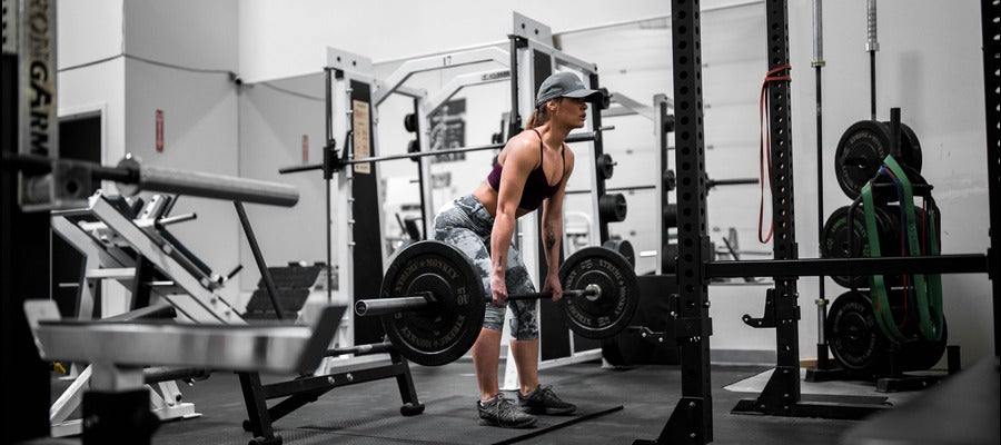 closeup of woman in a cap and top lifting barbells at the gym with exercise equipment around her