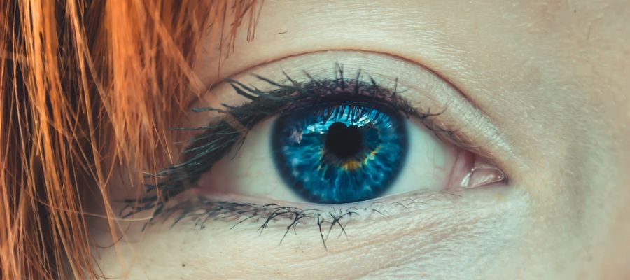 Primer plano de un ojo humano azul con pelo rojo a un lado.