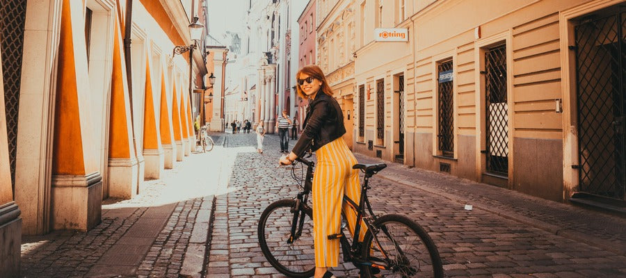 Mujer con bicicleta y gafas de sol en una calle adoquinada en el centro sonriendo mientras sostiene el manillar