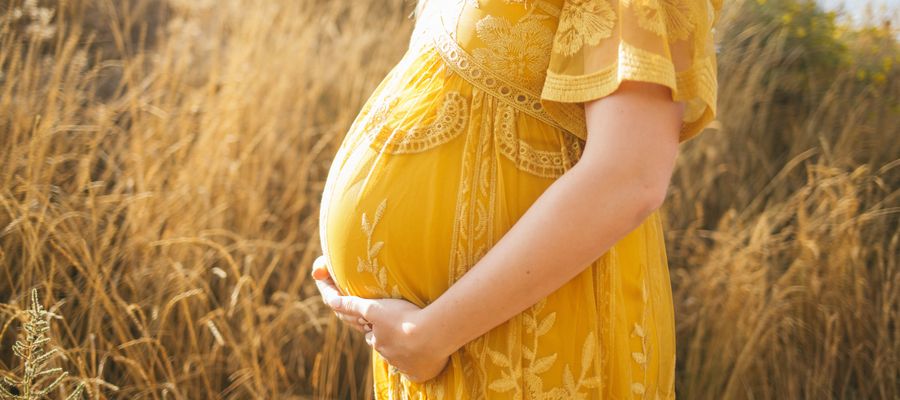 mujer embarazada con vestido amarillo sosteniendo su vientre de perfil contra el campo