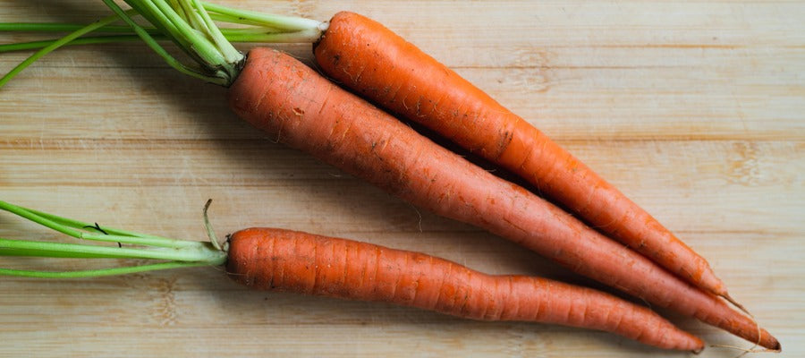 three large carrots with green stems on wooden table