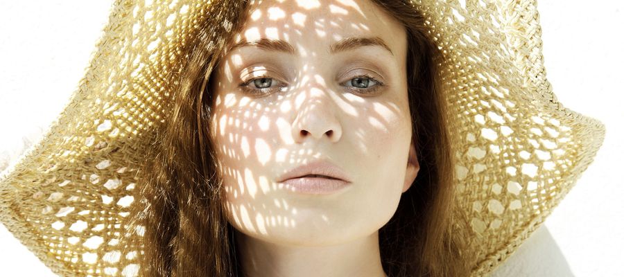 Mujer con sombrero de paja con la luz del sol tocando su rostro.