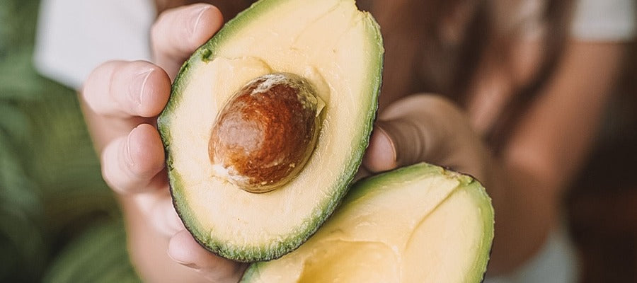 woman's hands holding sliced avocado