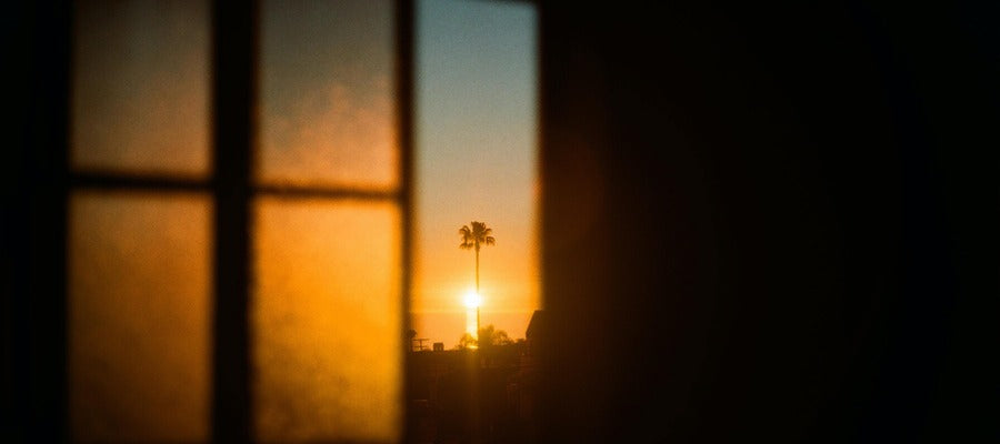 orange glow of senset seen through the narrow opening of a window in a darkening room