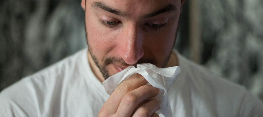 man in white shirt taking napkin to nose after having sneezed